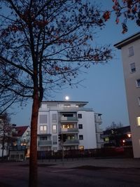 Illuminated street by buildings against sky at dusk