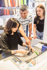 Instructor pointing at damaged mobile phone to young female trainee repairing at desk in store