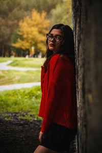 Side view of young woman standing by tree trunk