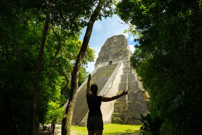 Rear view of woman standing against old ruins amidst trees