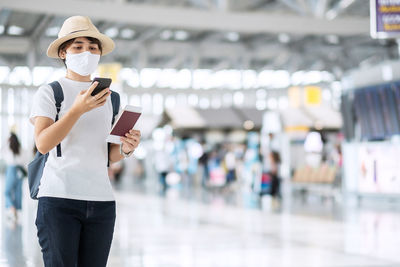 Woman wearing mask using phone standing at airport