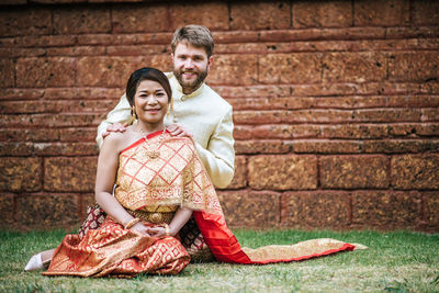 Portrait of couple sitting on grass against building