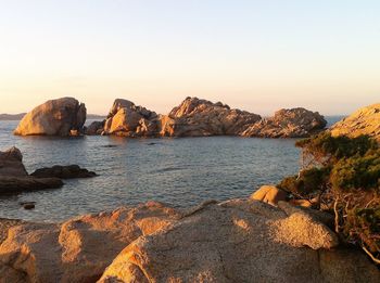 Rocks in sea against clear sky during sunset