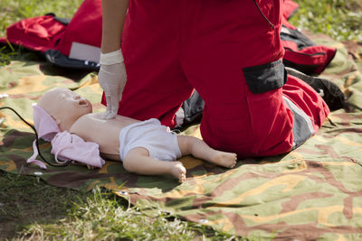 Low section of child with doll kneeling on blanket at park