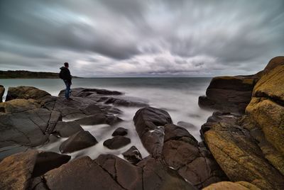 People standing on rocks by sea against sky