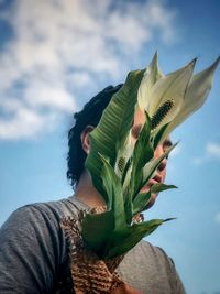Close-up of man holding peace lily flowers against cloudy sky.