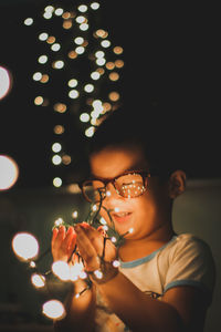 Close-up of young woman holding illuminated lamp at home