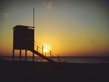 Silhouette built structure on beach against sky during sunset