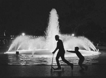 Silhouette people standing on illuminated shore against sky at night