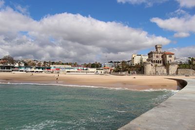 View of buildings by sea against cloudy sky