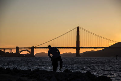 Silhouette of suspension bridge over sea