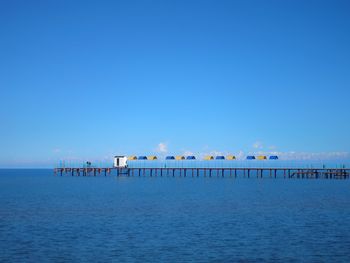 Pier over sea against clear blue sky