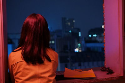 Rear view of woman standing by widow looking at view