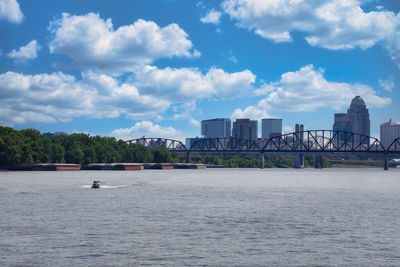 Bridge over river by buildings in city against sky