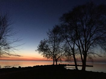 Silhouette bare trees on beach against sky at sunset