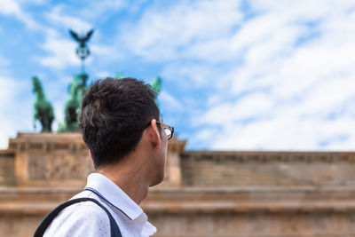 Side view of man looking away against sky in city