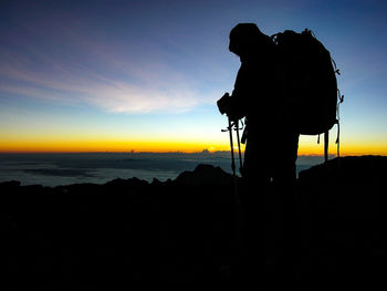 Silhouette person photographing at camera against sky during sunset
