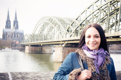 Portrait of smiling young woman against river in city