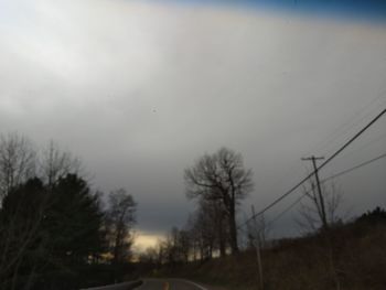 Silhouette bare trees by road against sky at dusk