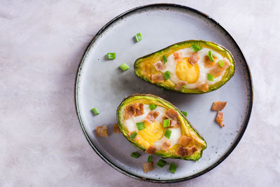 Close up of baked avocado with egg, bacon and chives on a plate for a keto diet top view