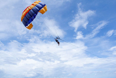 Low angle view of people paragliding against sky