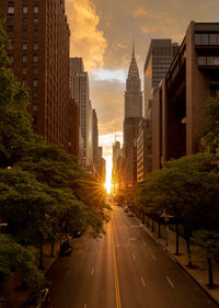 Road amidst buildings against sky during sunset