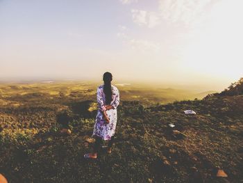 Rear view of woman standing on land against sky during sunset