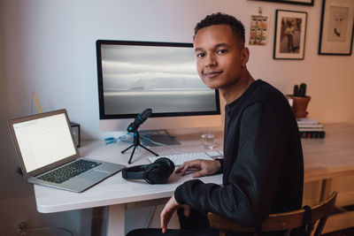 Portrait of confident young freelance worker sitting at desk with technologies