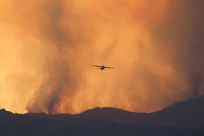 Low angle view of silhouette airplane flying against sky during wildfire