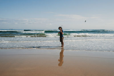 Full length of man playing violin standing on beach against sky