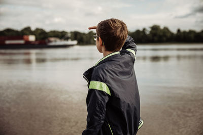 Rear view of man standing by lake against sky