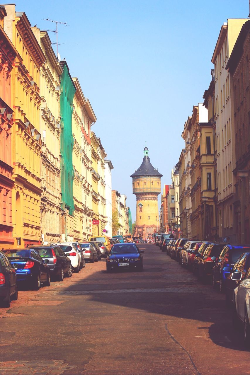 building exterior, architecture, built structure, car, transportation, street, land vehicle, city, mode of transport, road, clear sky, the way forward, city street, incidental people, blue, city life, diminishing perspective, parking, building, in a row