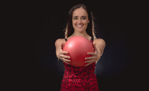 Portrait of mid adult woman holding fitness ball against black background