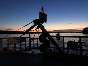 Silhouette crane by sea against sky at sunset