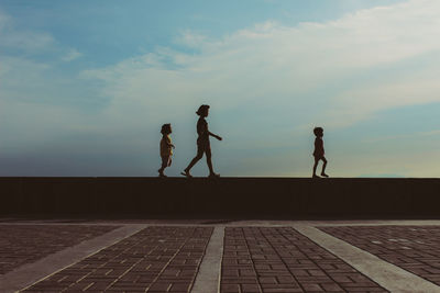 Side view of children walking on retaining wall against sky