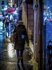 Rear view of woman walking on wet street in city