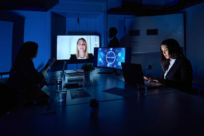 Colleagues working on laptops during online conference in dark office