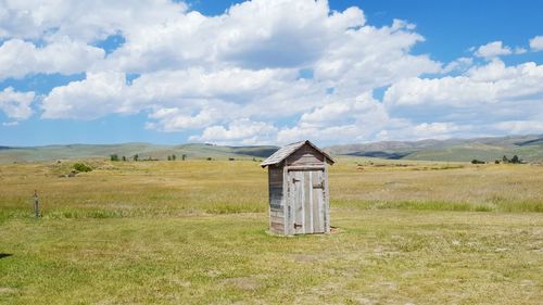Outhouse on grassy landscape against sky