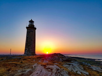 Lighthouse by sea against sky during sunset