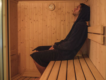 Side view of young man sitting on wooden wall