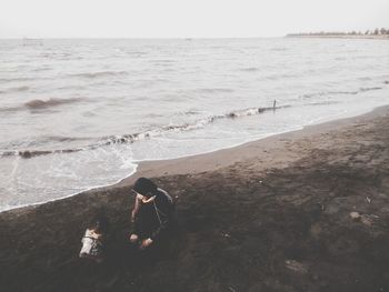 People sitting on shore at beach against sky