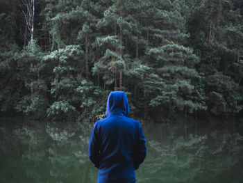 Rear view of man standing by calm lake with trees reflection