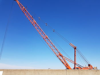 Low angle view of cranes against clear blue sky