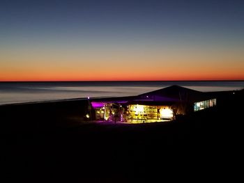 Illuminated built structure by sea against clear sky at night