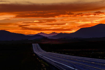 Road by silhouette mountains against orange sky
