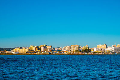 Sea by buildings against blue sky