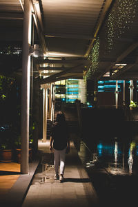 Rear view of woman walking in illuminated corridor