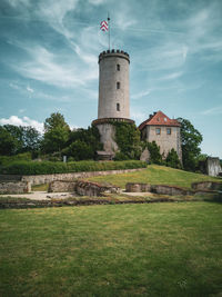 Lighthouse on field by building against sky