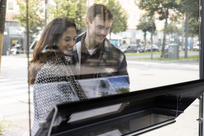 Happy young couple looking at placard on glass window of real estate office