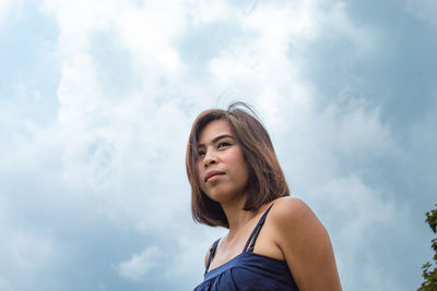 Low angle view of thoughtful woman standing against cloudy sky